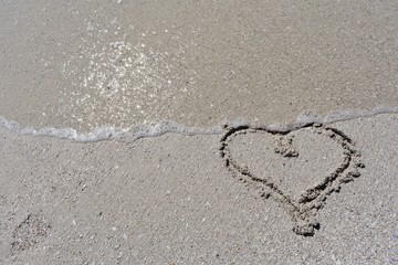 Heart drawn in the sand being washed away by a wave
