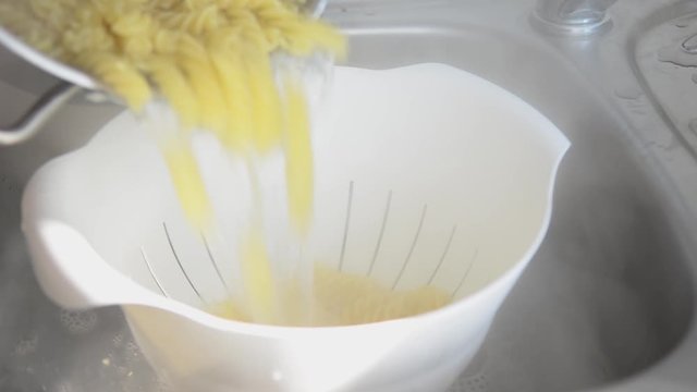 straining noodles on the white plastic drainer in the kitchen sink. close up