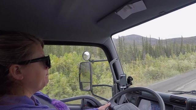 Woman with sunglasses driving commercial work truck down dirt road. Dempster Highway, Yukon, Canada.
