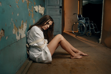 Obraz na płótnie Canvas Mad patient in straitjacket sitting on the floor