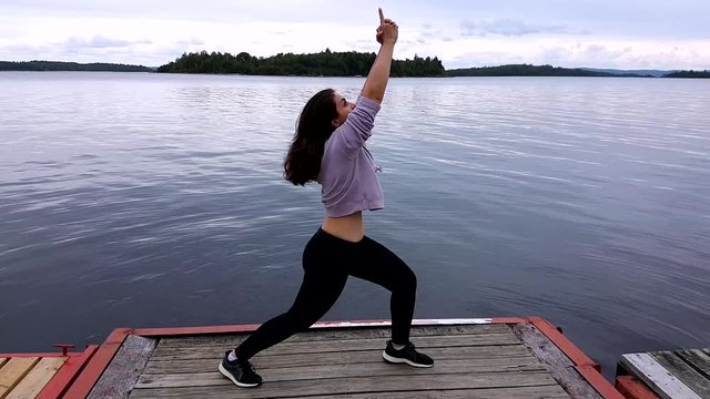 close shot of a lady standing on the wooden path in the sea doing a karate acting,facing side, bend one knee,hands up pointing finger  upwards .