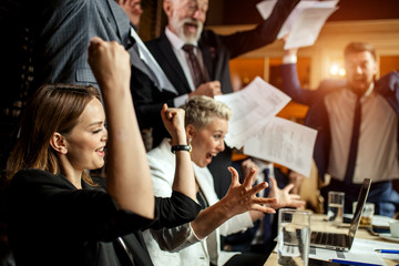 Group of professionals enthusiastically celebrating good deal consummation, raising hands up,...