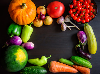 Autumn still life with pumpkin, watermelon, and a variety of colorful vegetables on black wooden background. Happy Thanksgiving background with copy space. Fresh organic food, close up.