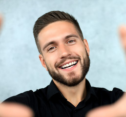 Obraz premium Chearful stylish man on grey background is taking a selfie