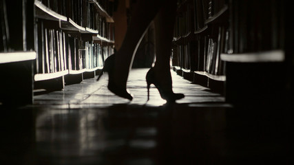 Beautiful librarian goes along the rows of books in libraries