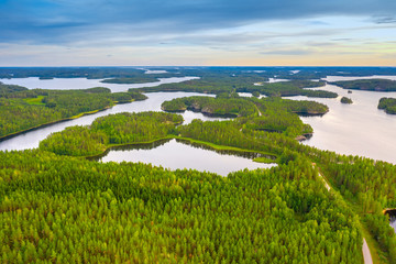 Aerial view of road between green summer forest, islands and blue lake in Finland.