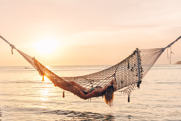 Girl relaxing in hammock on sunset beach