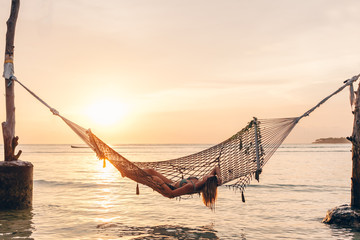 Girl relaxing in hammock on sunset beach