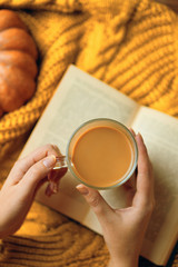 Mug of coffee, cozy knitted jacket, autumn, open book and pumpkin on wooden board. Autumn still life, vintage style. Flat lay.