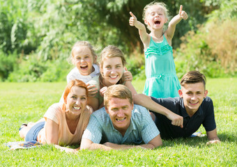 Portrait of big ordinary family lying on green lawn outdoors