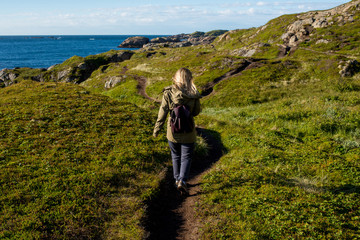 Woman goes on tourist hiking trail along ocean and mountains in Norway. Active recreation, healthy lifestyle. Enjoys scenic view. Beautiful nature. Travel, adventure. Sense of freedom. Explore North