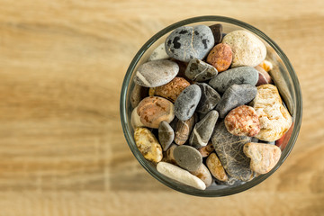Small sea stones in a glass vessel. The idea of decorating the house with small rocks in a jar on a wooden blurred background.