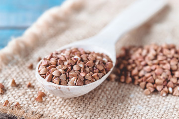 Uncooked buckwheat in a spoon on burlap background. Buckwheat is used for cooking.