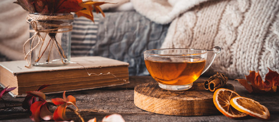 Cozy autumn or winter at home. A cup of tea, autumn casts a book a garland on a wooden table near a bed with warm plaids. Lifestyle autumn hygge lagom?concept of a holiday and autumn weekend.Banner