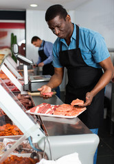 African American seller preparing fresh meat of lamb for sale in butcher store