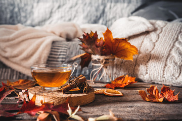 Cozy autumn or winter at home. A cup of tea, autumn casts a book a garland on a wooden table near a bed with warm plaids. Lifestyle autumn hygge lagom?concept of a holiday and autumn weekend.