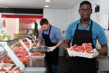 Fototapeta na wymiar Skillful butcher with colleague working behind counter