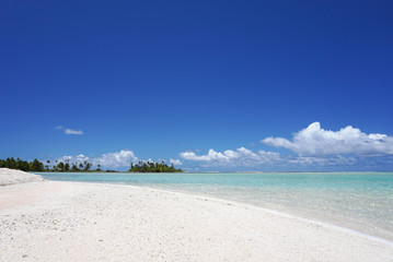 Turquoise water washes up on a white sandy beach with palm trees on a tropical island