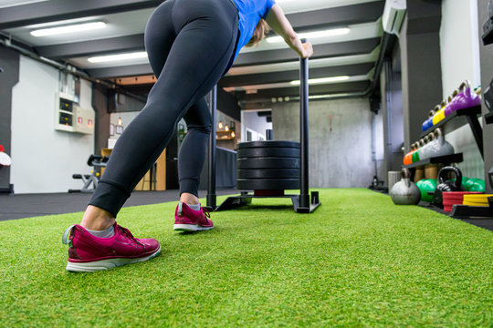 Low Angle View Of Female Pushing Sled In Local Gym.