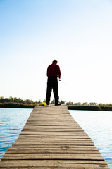 Fototapeta na wymiar fisherman on a bridge near a blue lake