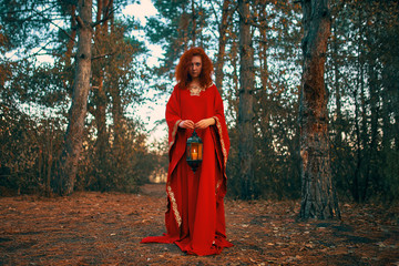 Obraz na płótnie Canvas Woman in red holding a lantern with a candle. Hand lantern with a candle shines in the woods.