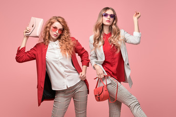Fashionable autumn woman with stylish hairstyle, makeup dance. Two Shapely blonde redhead girl having fun, trendy red outfit, heels, fashion hair, make up. Excited model, autumnal beauty pink concept