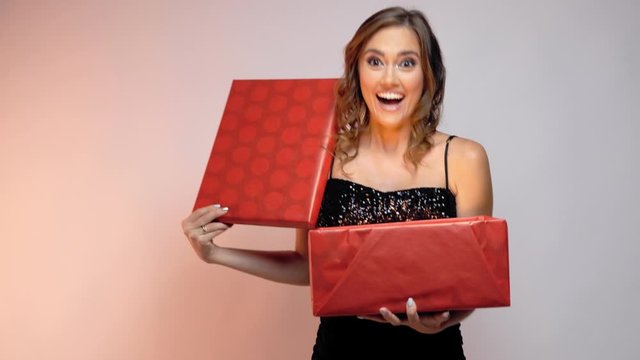 Young woman opening a red box with shiny magic gift inside.