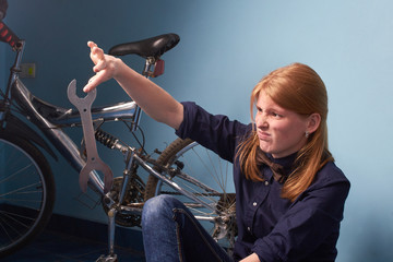 Plakat girl repairs the bike.pretty girl sitting on the floor of a bike shop and does not know what to do with the tool