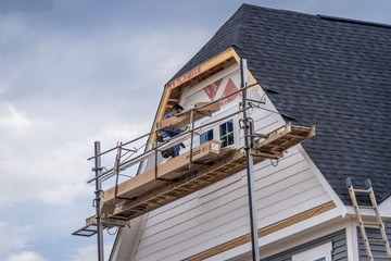 Carpenter on scaffolding installing white vinyl siding on a new construction American single family home in the USA - obrazy, fototapety, plakaty
