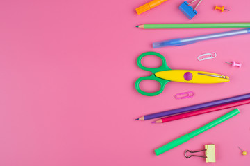 Colorful school supplies over a paper on pink background with place for your text