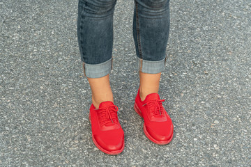 Female legs in red sneakers and jeans pants. Leather sport wear.