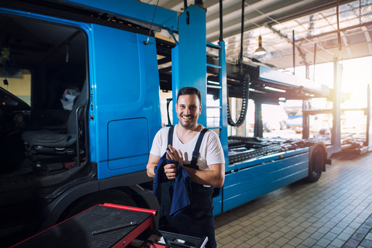 Smiling professional truck serviceman holding rug and cleaning hands after successfully finishing truck service and maintenance.