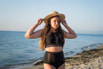 Fototapeta na wymiar Cheerful plus size teenage girl wearing hat enjoying the beach. smiling, happy, positive emotion, summer style.