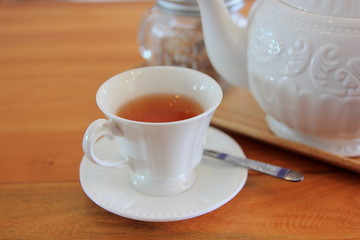 Tea pot in white cup and brown wooden background.