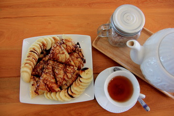Banana Roti with Chocolate Topping and milk in white disc on brown wooden table. 