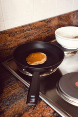 Pancake cooking in a black pan in a kitchen