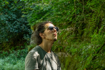 Walk outdoors. A young man in sunglasses looks at the nature around him. Sunlight falls on the face.