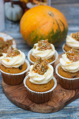 Pumpkin cupcakes with cream cheese frosting decorated with pecan nuts, maple syrup, caramel bites and chocolate toffee candies on wooden rustic background
