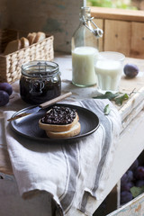 Bread toast with plum jam, served with milk and plums on a wooden background. Rustic style.