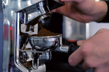 Barista grinding coffee beans using coffee machine and holder.