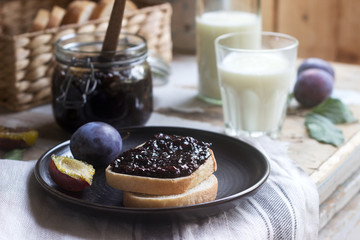 Bread toast with plum jam, served with milk and plums on a wooden background. Rustic style.