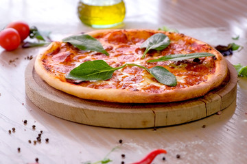 Salami pizza with spinach leaves served on wooden board on the table. Close-up side view