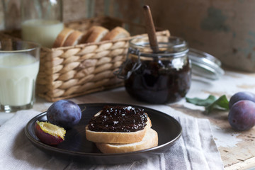 Bread toast with plum jam, served with milk and plums on a wooden background. Rustic style.