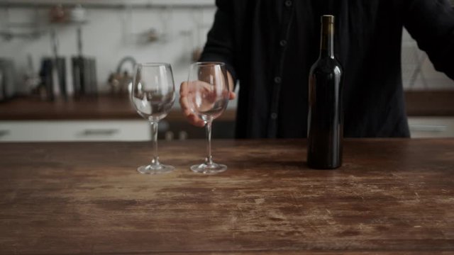 young guy opens a bottle of wine in the kitchen with a corkscrew
