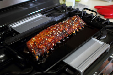 Marinated St. Louis cut pork ribs baked on a carbon steel tray, resting on the stove top in a home kitchen.