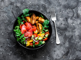 Smoked salmon, baked potatoes, fresh vegetables salad breakfast bowl on a dark background, top view