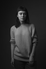 Portrait of young woman in sweater on black background. Black and white
