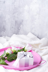 Fototapeta na wymiar Gift box and pastel flowers eustoma for Valentines or Mothers day on pink tray on bed . Flat lay style.