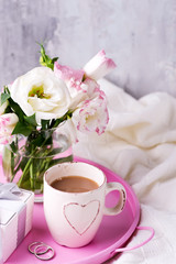 Having a cup of coffee with chocolate, flowers eustoma and gift box on tray on blanket in bed. Holiday concept