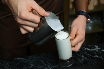 Fototapeta na wymiar Barista pouring milk into glass cup for coffee drink at table